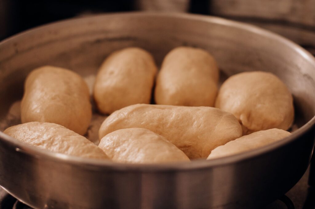 Gros plan de petits pains fraîchement levés dans un plateau de cuisson, mettant en valeur des croûtes dorées.