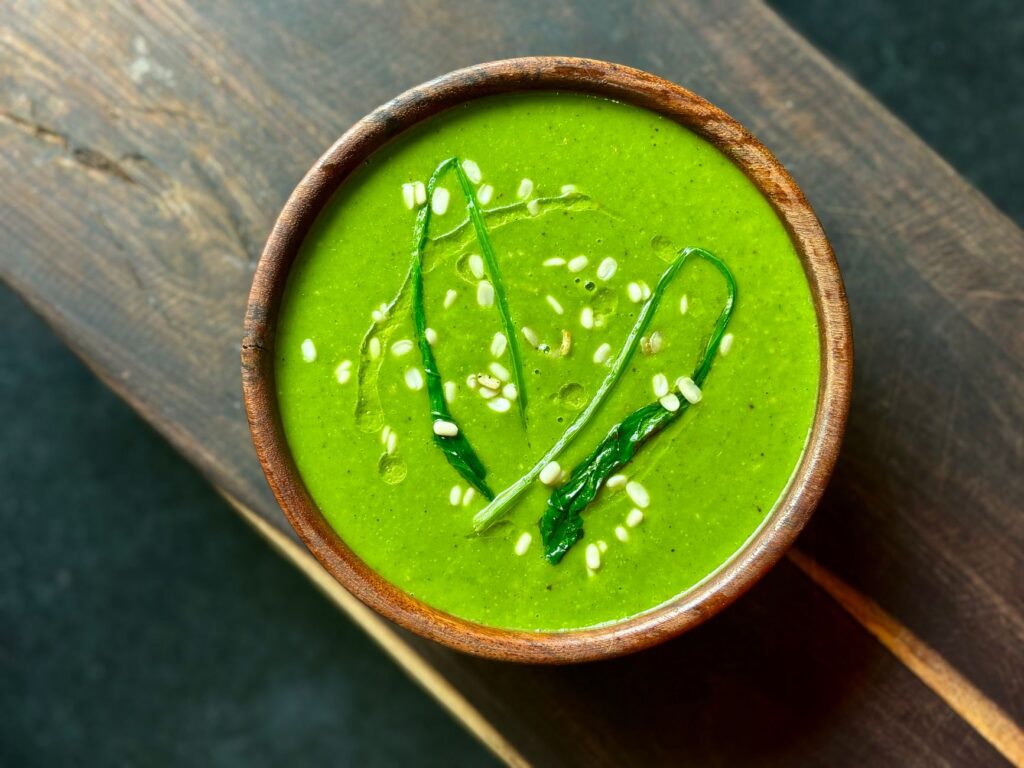 Délicieuse soupe d'épinards garnie de graines de sésame et de légumes verts, servie dans un bol en bois rustique.