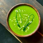 Délicieuse soupe d'épinards garnie de graines de sésame et de légumes verts, servie dans un bol en bois rustique.