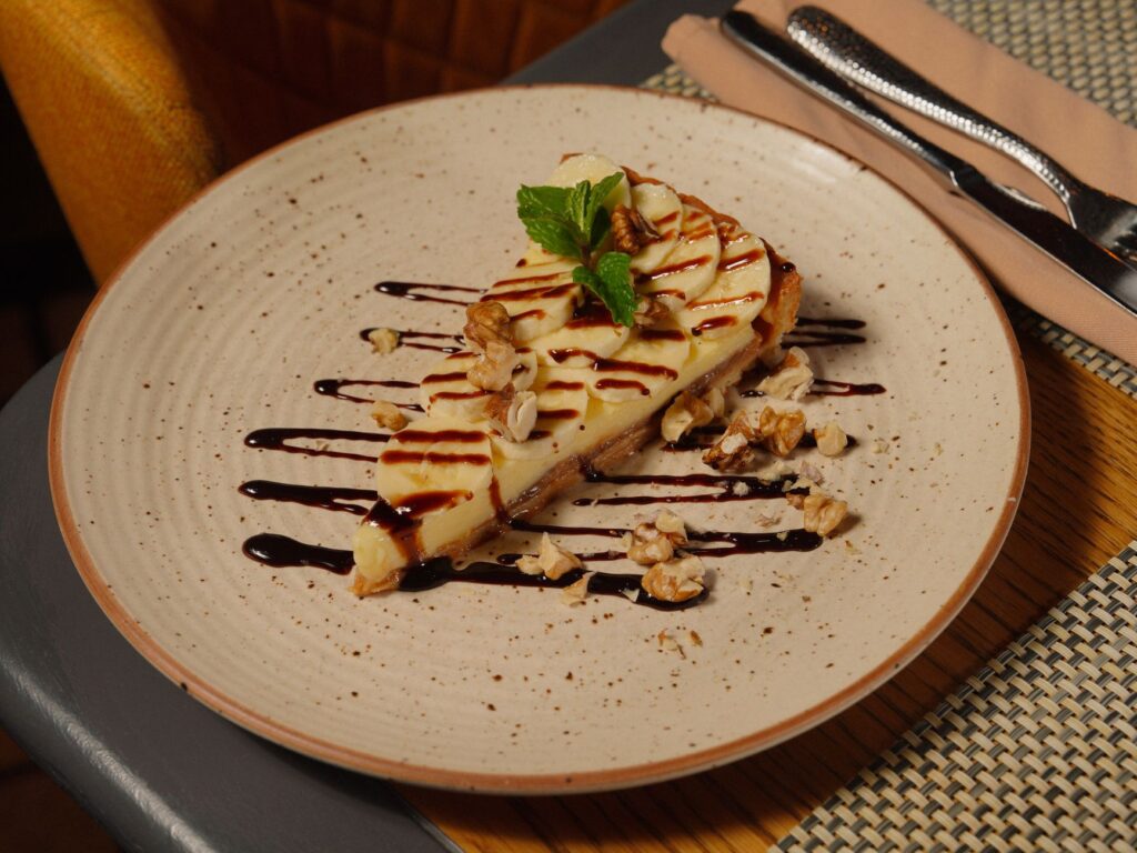 Une part de cheesecake crémeux garnie de noix et de menthe, arrosée de sauce au chocolat.