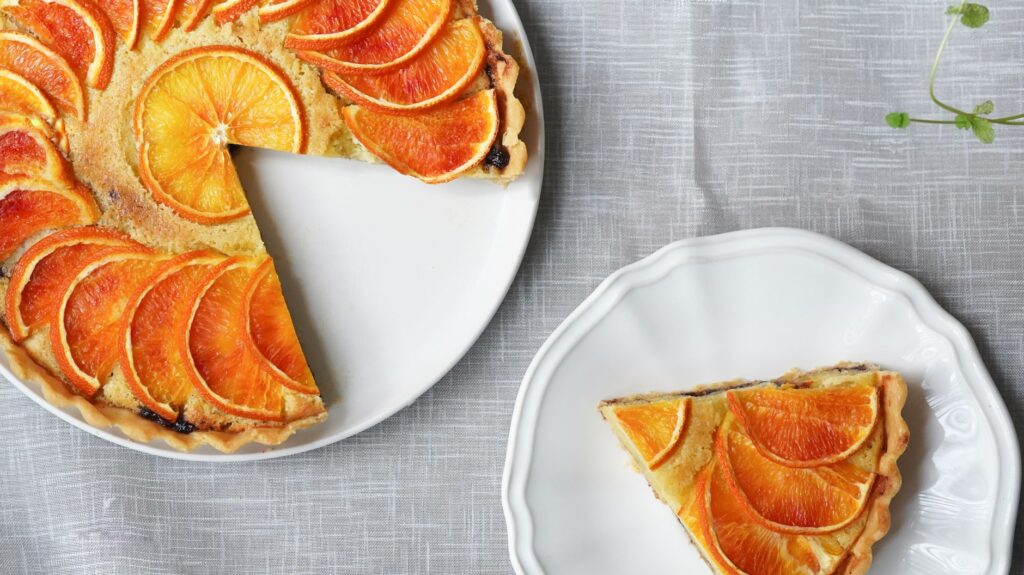 Tarte aux agrumes orange fraîchement cuite avec une part servie sur une assiette blanche.