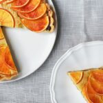 Tarte aux agrumes orange fraîchement cuite avec une part servie sur une assiette blanche.