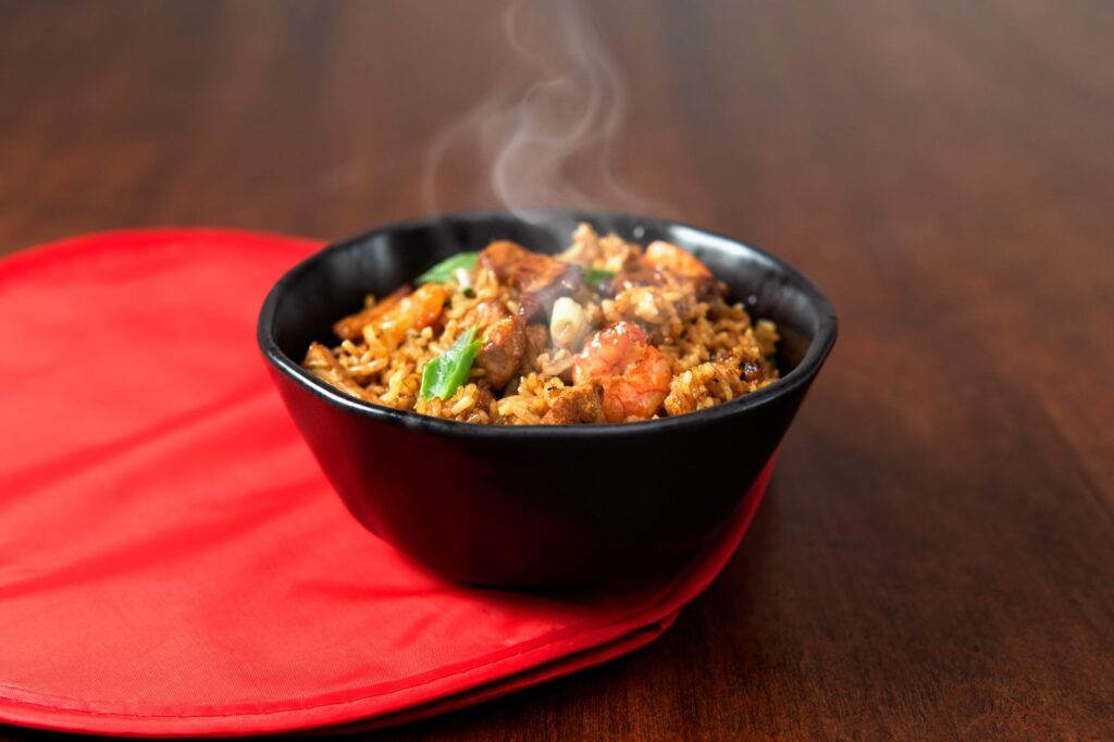 Gros plan sur du riz frit asiatique fumant dans un bol noir sur un tapis rouge. Parfait pour les passionnés de photographie culinaire.