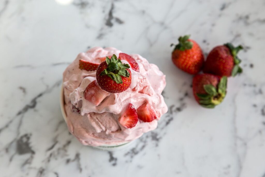 Un bol de glace maison à la fraise avec des fraises fraîches sur un plan de travail en marbre.