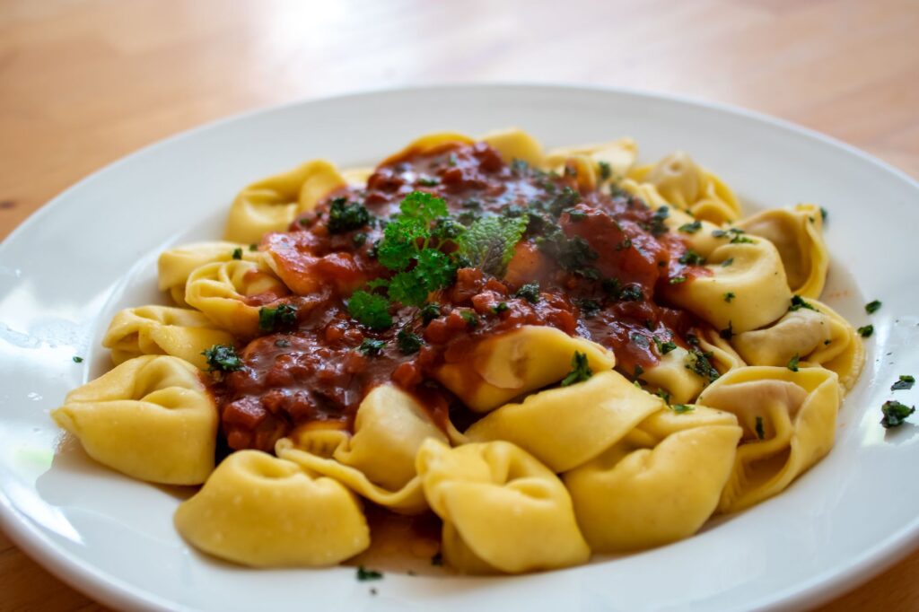 Gros plan de tortellini avec une sauce tomate basilic riche sur une assiette blanche.