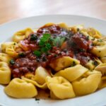 Gros plan de tortellini avec une sauce tomate basilic riche sur une assiette blanche.