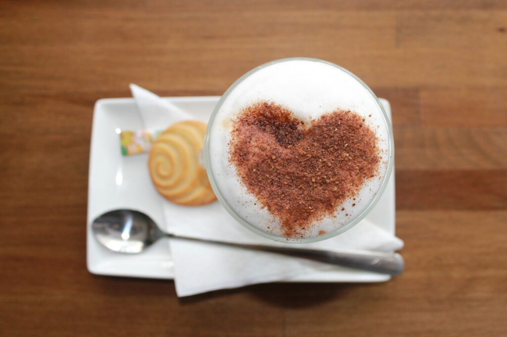 Un cappuccino mousseux décoré d'un cœur en cacao servi avec un biscuit sur une table en bois.