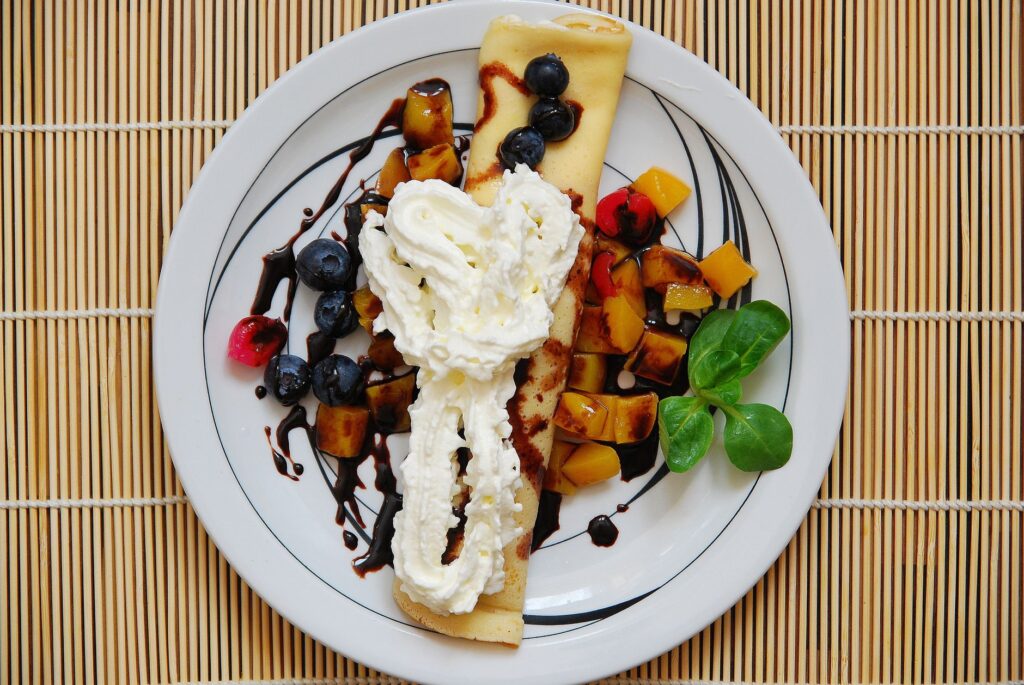 Une crêpe délicieuse garnie de fruits frais et de crème, servie dans une assiette élégante, parfaite pour un petit-déjeuner sucré.
