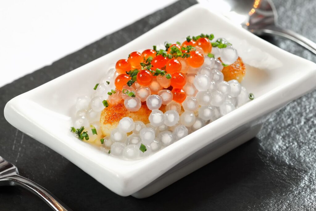 Gros plan sur un plat gastronomique avec du caviar vibrant et des perles de tapioca translucides, joliment présenté.