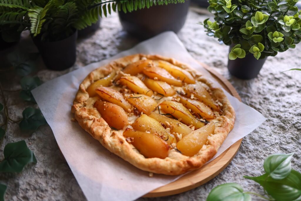 Appétissant tarte rustique aux poires faite maison servie sur du papier parchemin, entourée de légumes frais.
