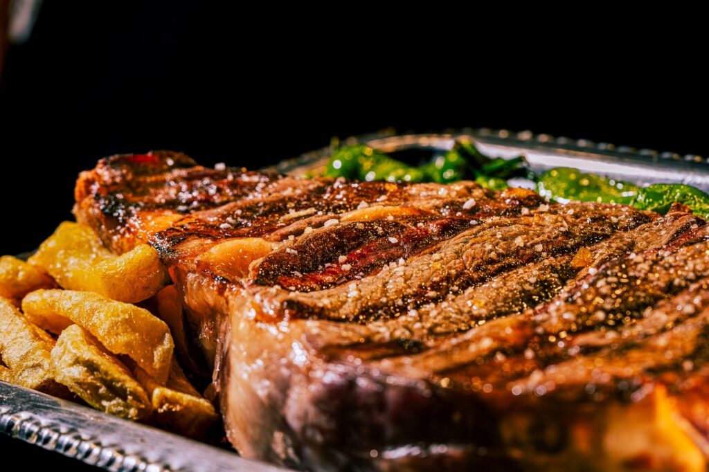 Gros plan sur un juteux steak ribeye grillé avec des épices et des accompagnements sur un plateau en argent.