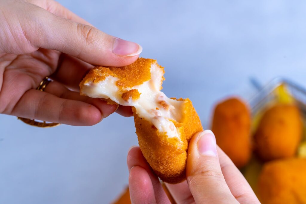 Gros plan sur une main cassant une croquette au fromage, mettant en valeur la garniture de fromage fondu.