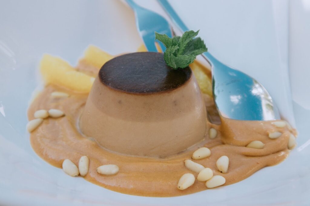 Gros plan sur une panna cotta crémeuse au caramel, garnie de menthe, servie avec une cuillère.