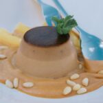 Gros plan sur une panna cotta crémeuse au caramel, garnie de menthe, servie avec une cuillère.