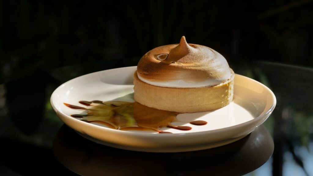 Tarte au citron meringuée avec sauce caramel sur une assiette blanche.