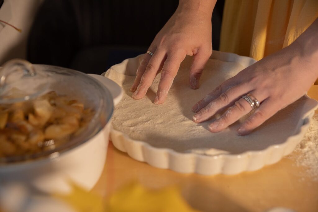 Mains façonnant la pâte dans un moule à tarte avec de la garniture aux pommes à proximité, parfait pour les passionnés de pâtisserie.