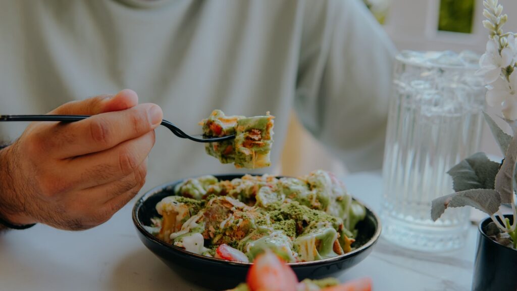 Gros plan sur une personne mangeant des pâtes à la sauce verte crémeuse à une table