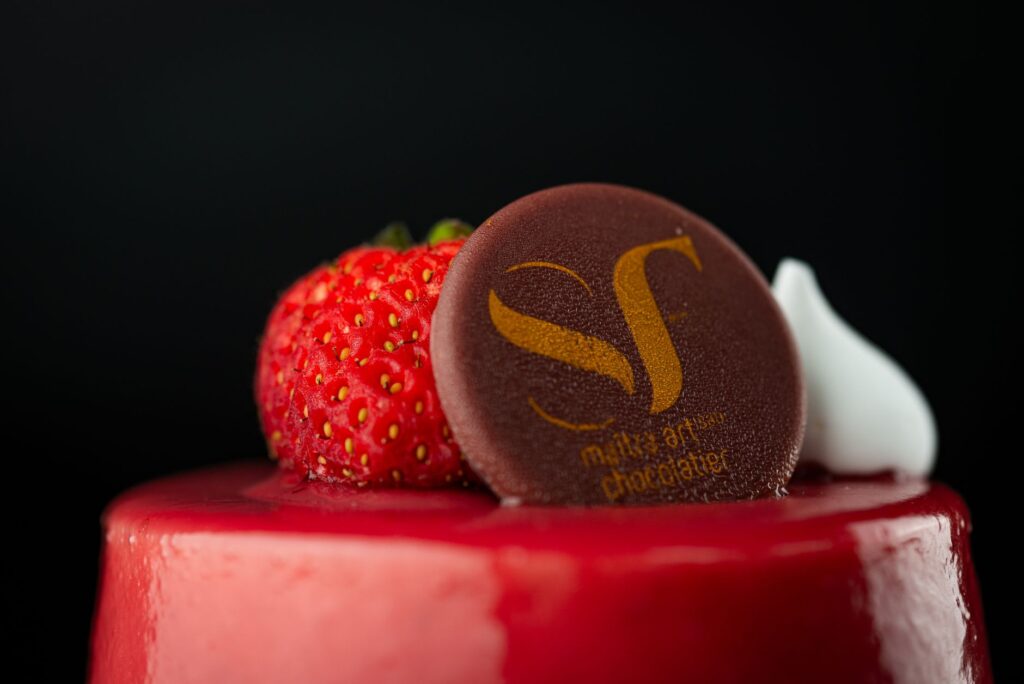 Gros plan d'un gâteau glacé rouge garni de fraises fraîches et d'un disque de chocolat de marque.
