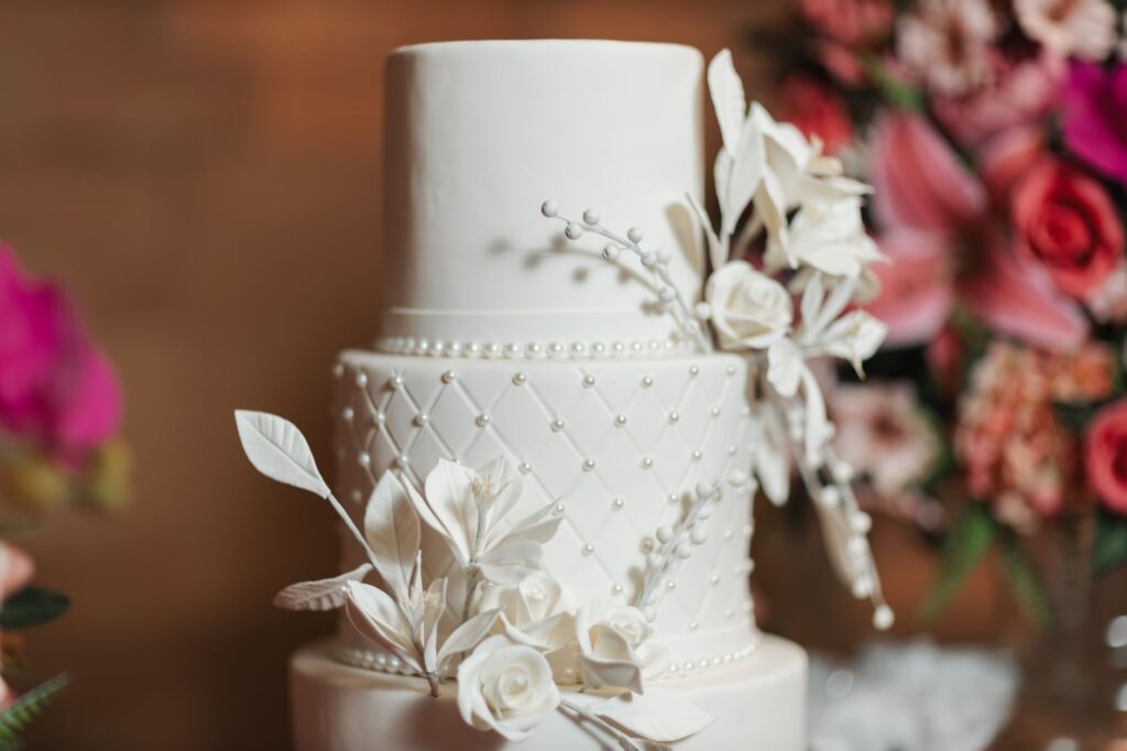 Un gâteau de mariage blanc à trois étages magnifiquement détaillé, orné de délicates fleurs blanches et de perles.