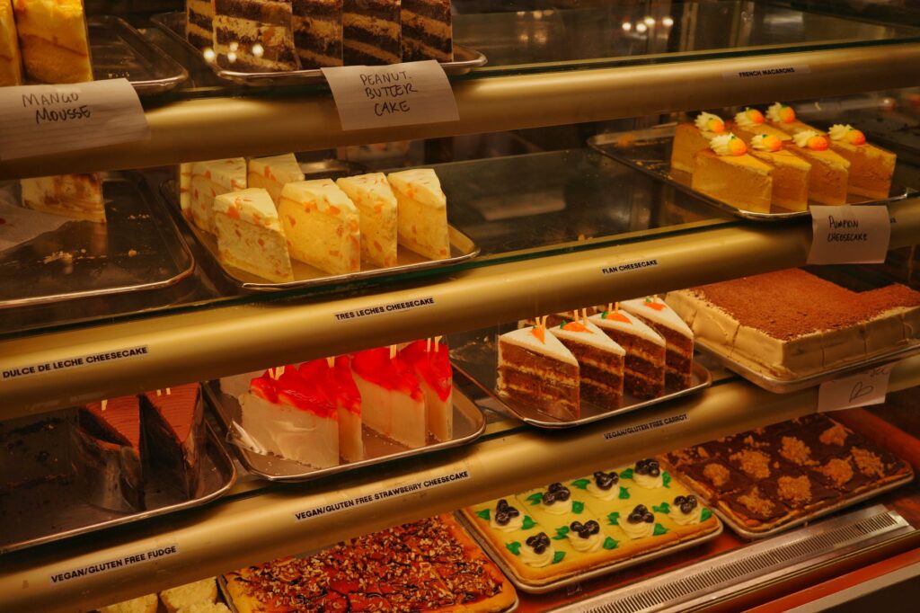 Une variété de gâteaux et de cheesecakes dans une vitrine de boulangerie, mettant en avant des saveurs diverses.