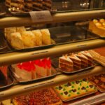 Une variété de gâteaux et de cheesecakes dans une vitrine de boulangerie, mettant en avant des saveurs diverses.