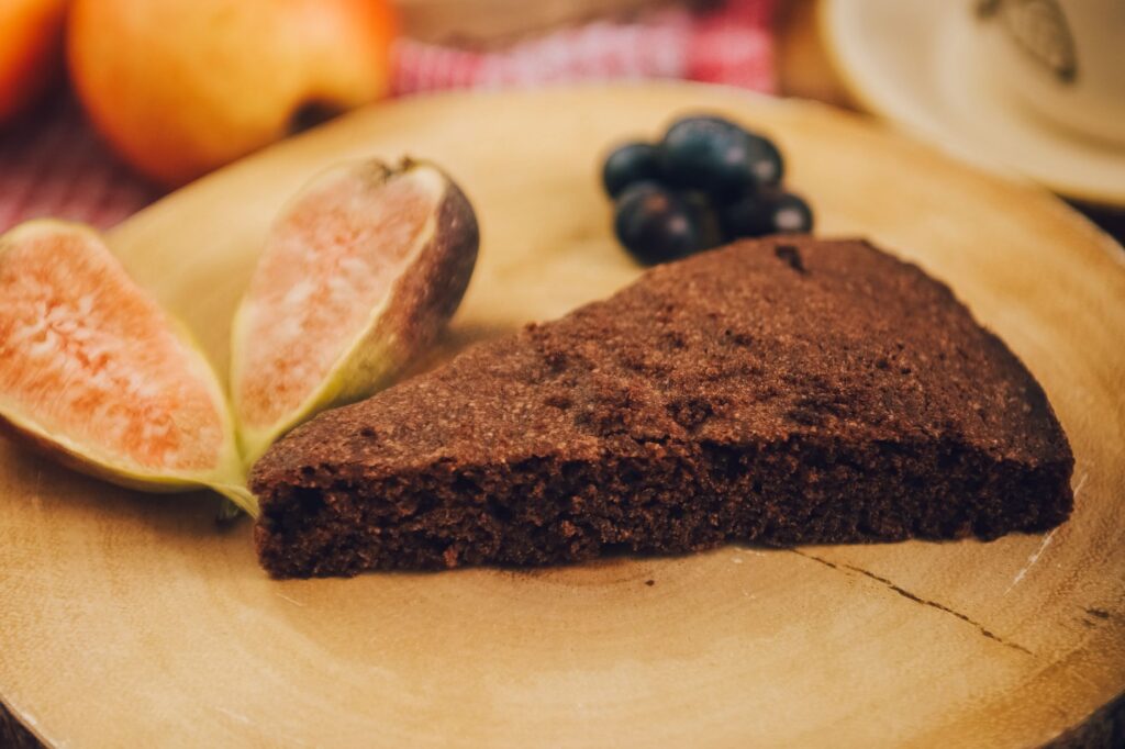 Une délicieuse tranche de brownie accompagnée de figues fraîches et de raisins sur un plateau en bois.