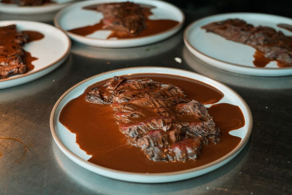 Picanha tranchée délicieusement cuite, servie avec une riche sauce barbecue sur des assiettes blanches, parfaite pour un dîner gastronomique.