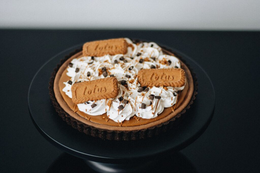 Une élégante tarte aux biscuits au caramel joliment présentée sur un piédestal noir, parfaite pour les présentations gastronomiques.