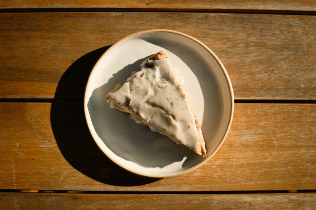 Un scone rustique avec du glaçage sur une assiette, baignant dans une lumière naturelle chaleureuse sur une table en bois.