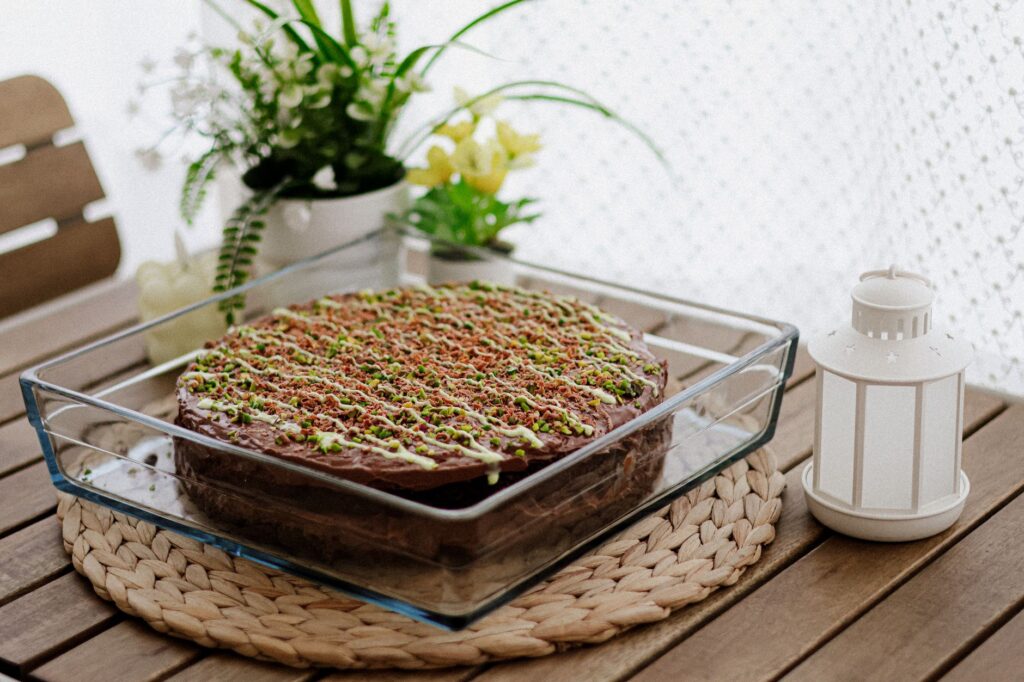 Un gâteau au chocolat fait maison, magnifiquement décoré et garni de pistaches dans un cadre chaleureux.