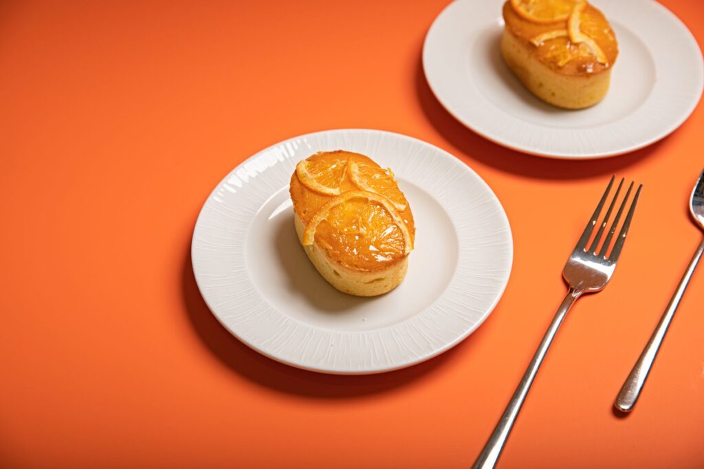 Délicieux gâteau glacé à l'orange servi sur une assiette blanche, accompagné de fourchettes sur un fond orange vif.