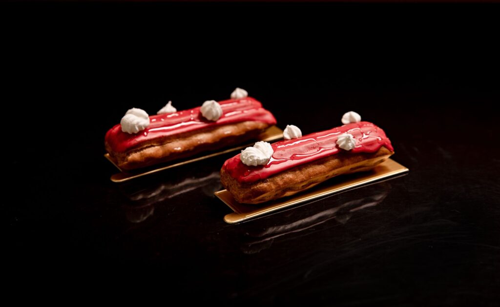 Deux éclairs glacés rouges gourmands avec garniture à la crème sur fond sombre.