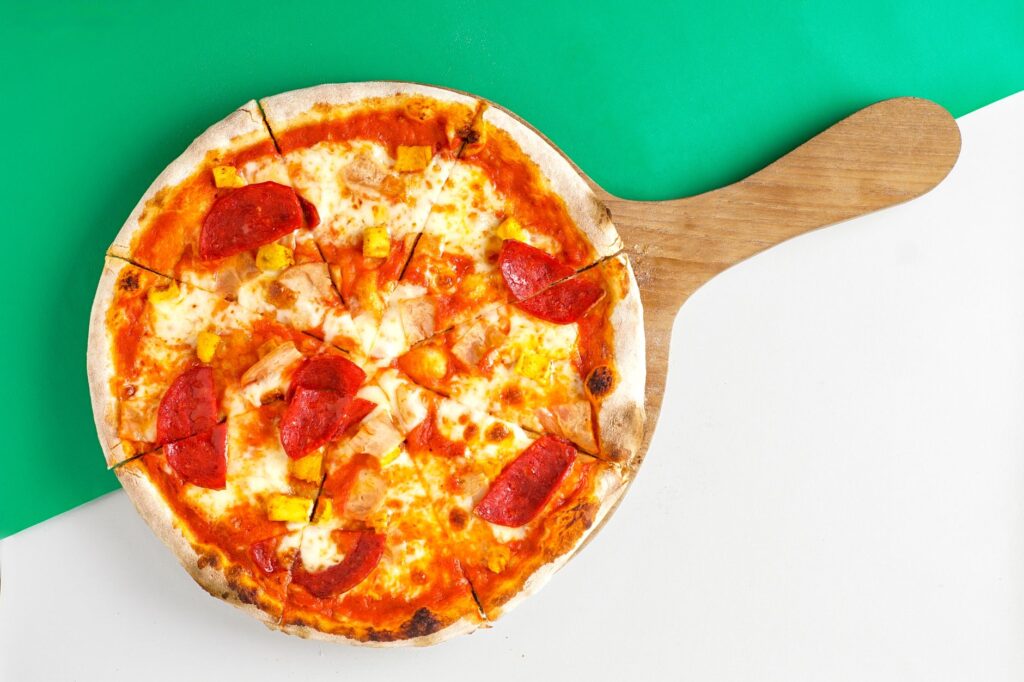 Vue de dessus d'une pizza au pepperoni et au fromage sur une planche de bois, prête à servir.