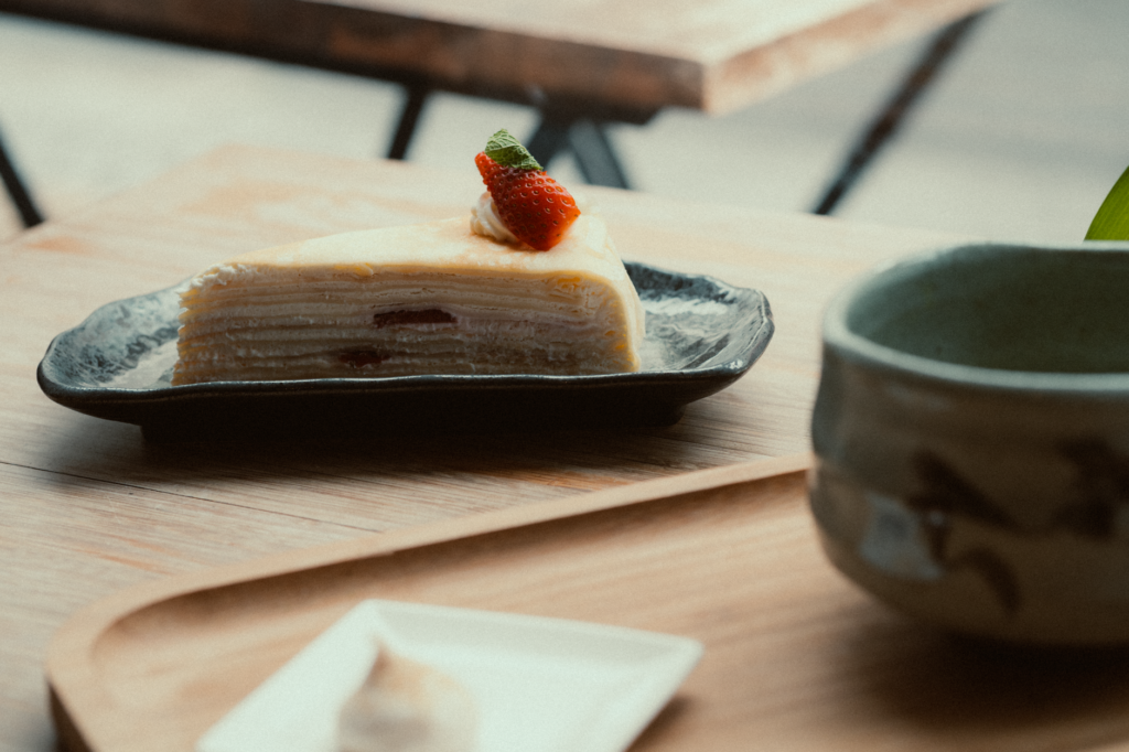 Une tranche de gâteau de crêpes garnie d'une fraise, servie sur une table en bois.