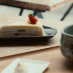 Une tranche de gâteau de crêpes garnie d'une fraise, servie sur une table en bois.