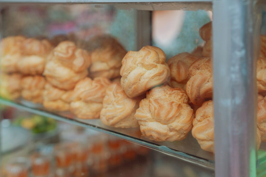 Choux à la crème fraîchement cuits empilés dans une vitrine de pâtisserie, mettant en valeur leur texture dorée et délicieuse.