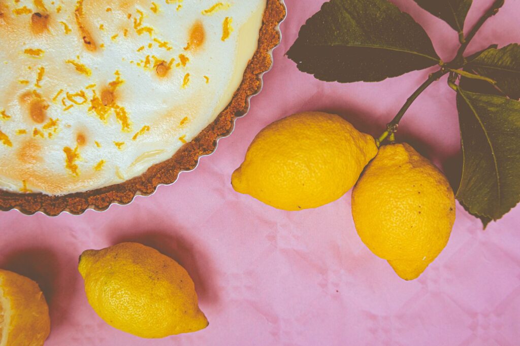 Élégante tarte au citron meringuée avec des accents de zeste et des citrons frais sur un fond rose vif.