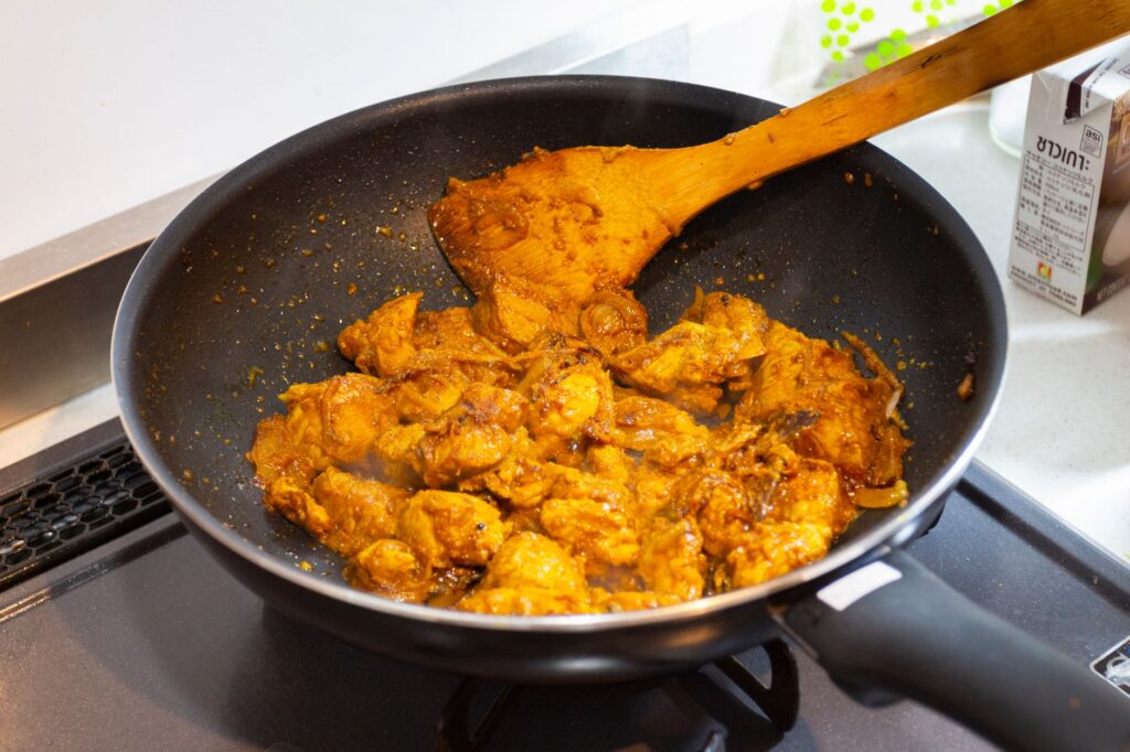 Une poêle remplie de poulet au curry épicé en train de cuire sur une cuisinière, présentant une riche teinte dorée.