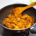 Une poêle remplie de poulet au curry épicé en train de cuire sur une cuisinière, présentant une riche teinte dorée.