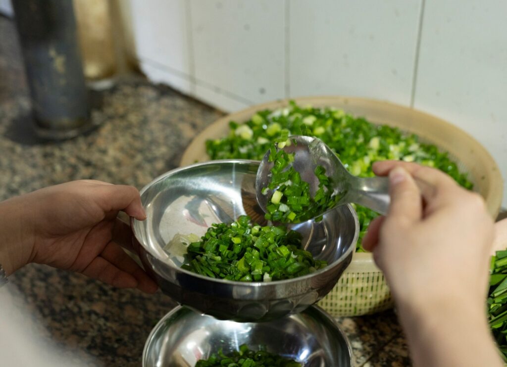 Gros plan de mains coupant des oignons verts frais dans une cuisine traditionnelle du Yunnan.