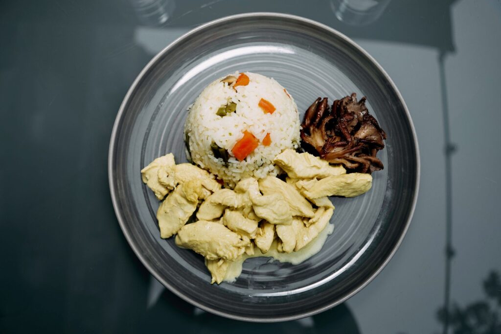 Un repas soigneusement préparé composé de poulet, de riz aux légumes et de champignons sur une assiette en céramique.