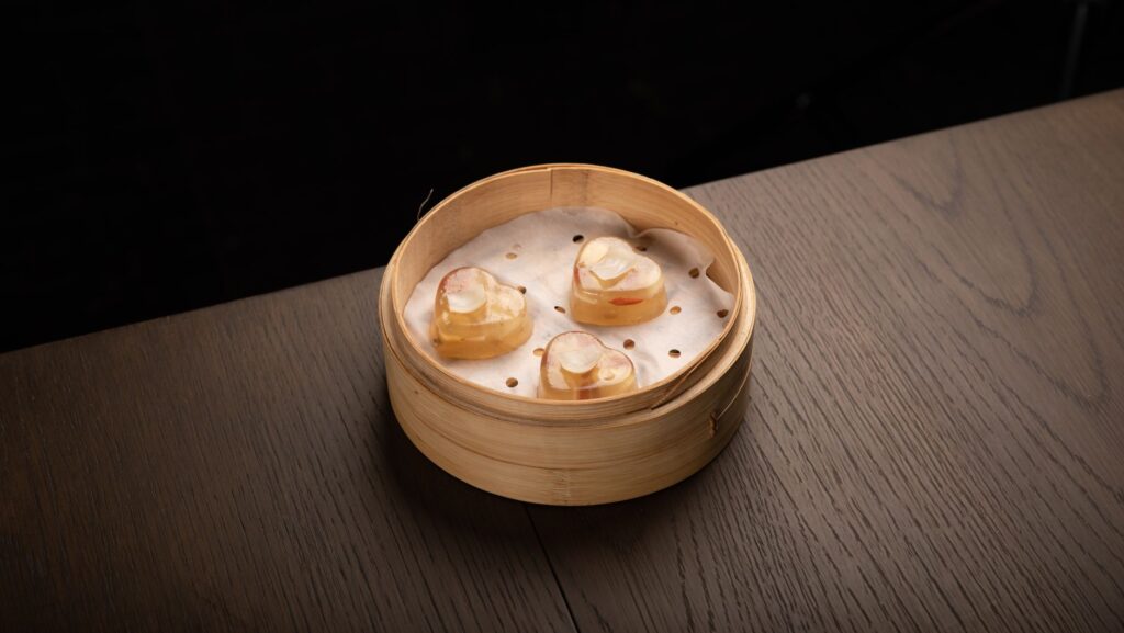Trois morceaux de dim sum en forme de cœur dans un cuiseur vapeur en bambou sur une table en bois.