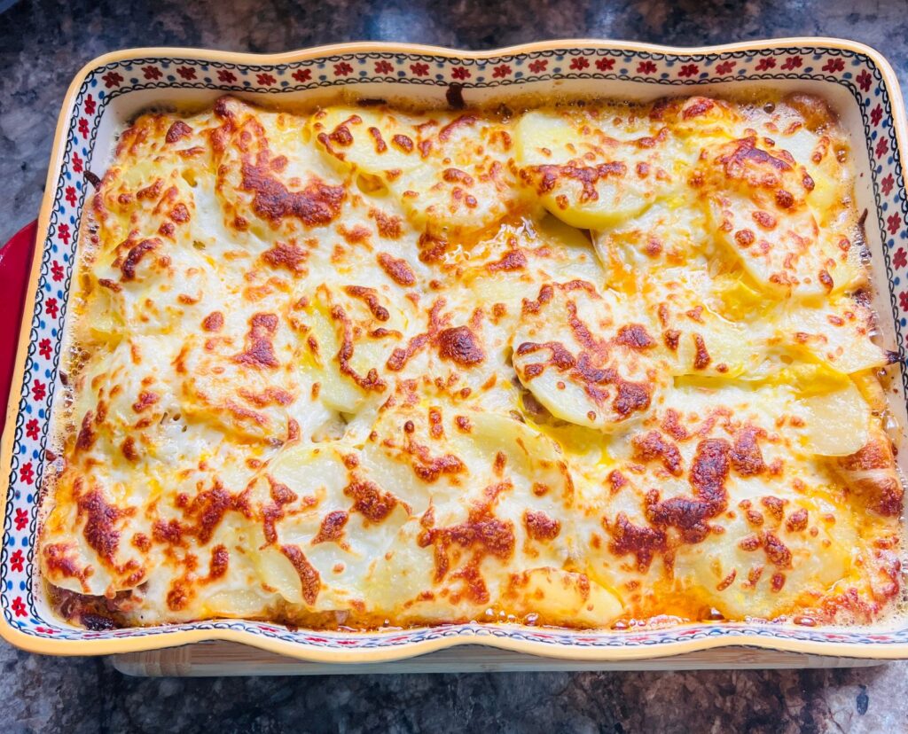 Délicieuse cocotte de fromage et de pommes de terre dorée dans un plat de cuisson décoratif.
