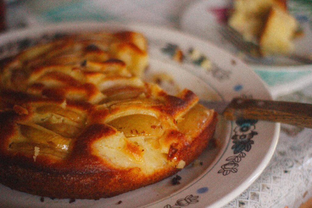 Gros plan d'une tarte aux pommes rustique faite maison sur une assiette à motifs vintage, évoquant une ambiance chaleureuse et confortable.