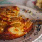Gros plan d'une tarte aux pommes rustique faite maison sur une assiette à motifs vintage, évoquant une ambiance chaleureuse et confortable.