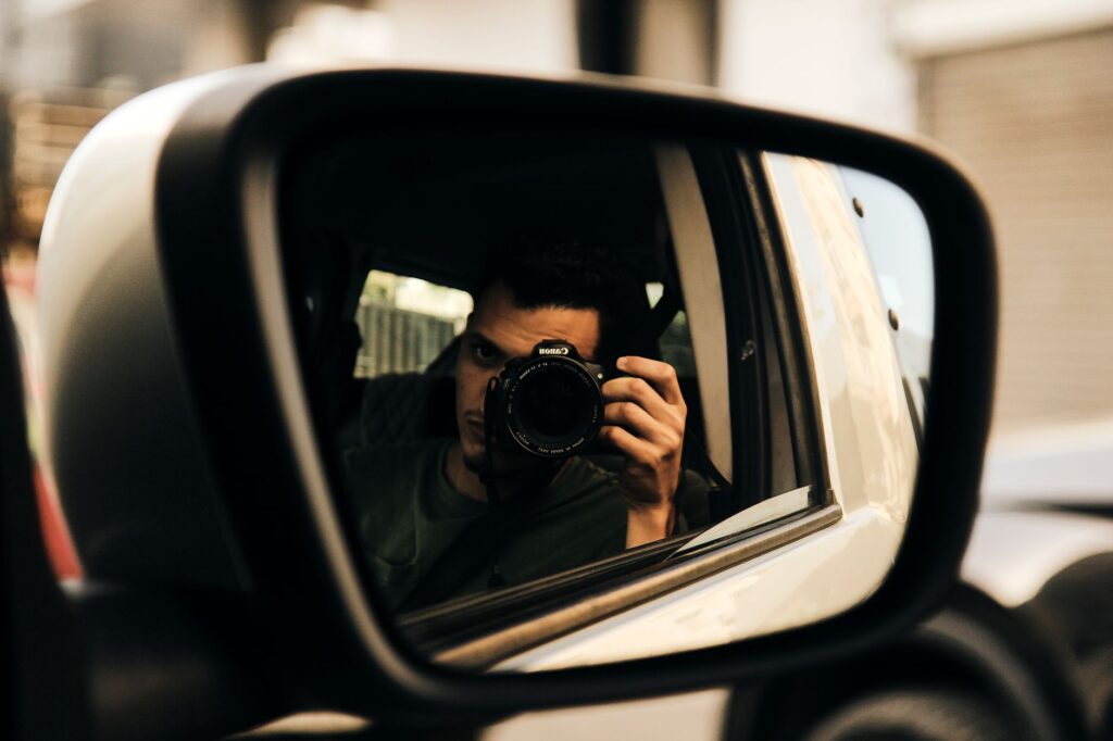 Un autoportrait créatif capturant un photographe à travers le reflet d'un rétroviseur latéral de voiture.