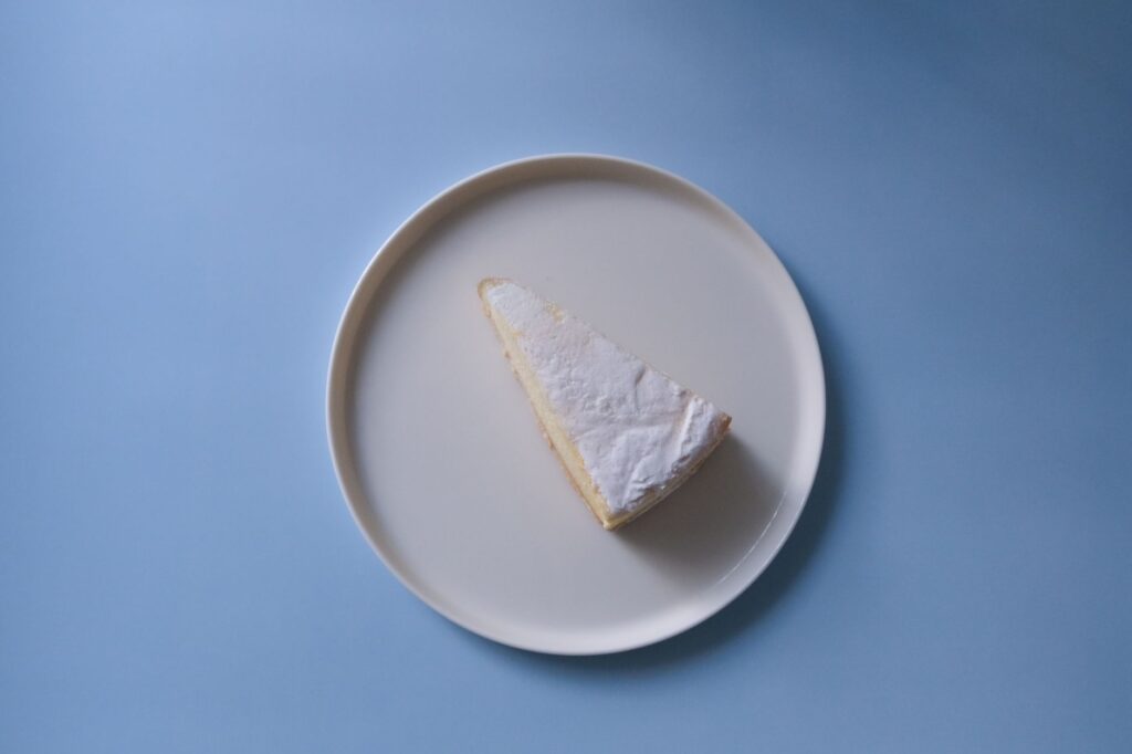 Une seule tranche de gâteau au citron saupoudrée de sucre glace sur une assiette blanche à fond bleu.