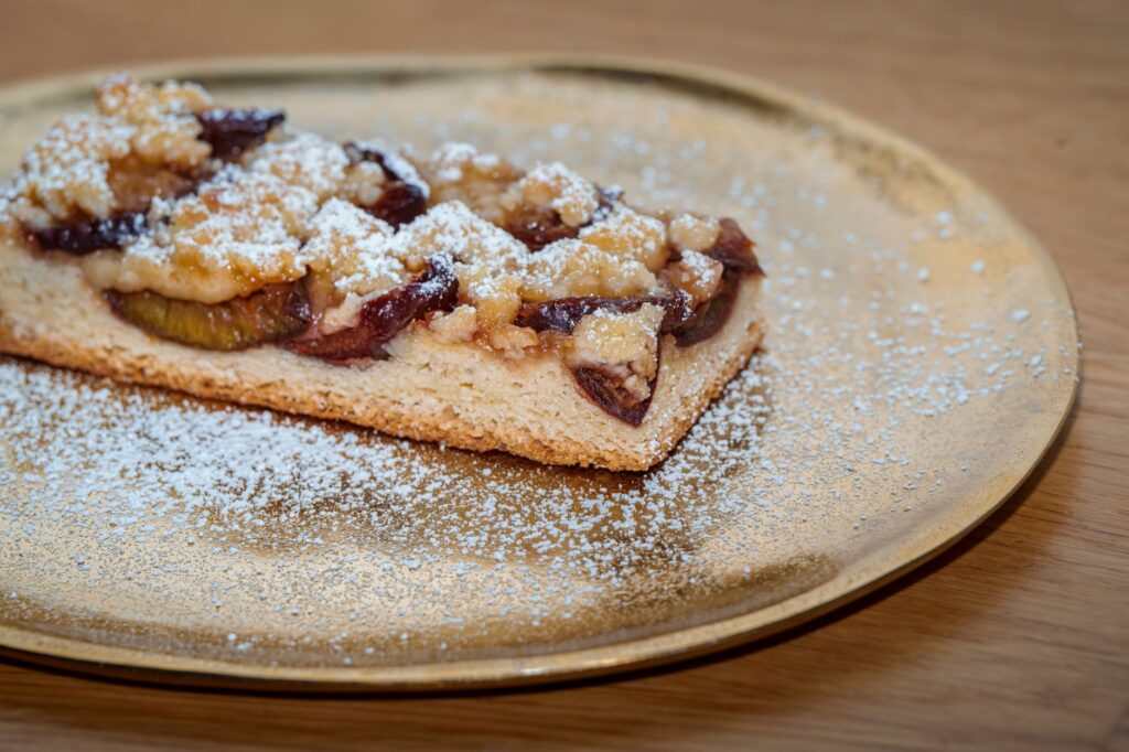 Tarte aux prunes avec un crumble sur une assiette dorée, saupoudrée de sucre glace.