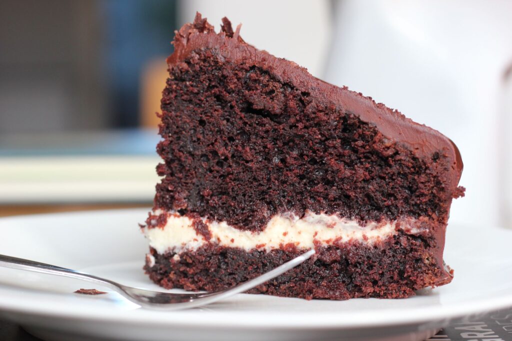 Gros plan d'une part de gâteau au chocolat riche avec une garniture crémeuse sur une assiette blanche.