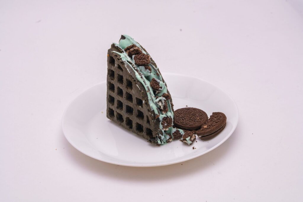 Délicieuse gaufre au chocolat et à la menthe accompagnée de biscuits, servie sur une assiette blanche, parfaite pour les amateurs de desserts.